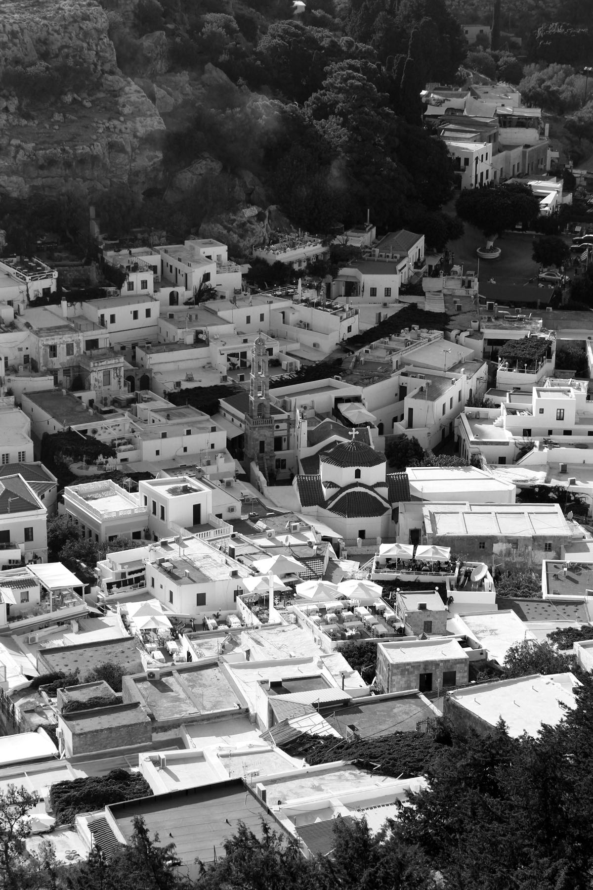 Black and white photo from on high, looking down at a cluster of buildings forming the small greek town, Lindos, Rhodes.